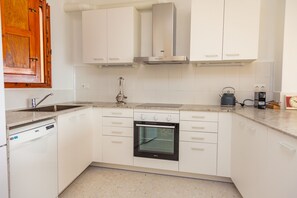 A kitchen with white cabinets, a dishwasher, an oven, a coffee maker, and a kettle. - Cullera Beachfront Apartment (Cullera)