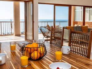 A wooden dining table with fruit and juice glasses, a wicker chair, and a sofa with cushions. - Cullera Beachfront Apartment (Cullera)