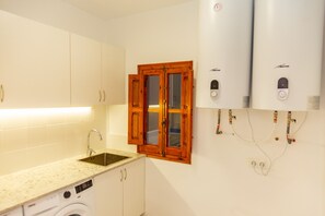 A kitchen with a sink, washing machine, wooden window, and two water heaters. - Cullera Beachfront Apartment (Cullera)