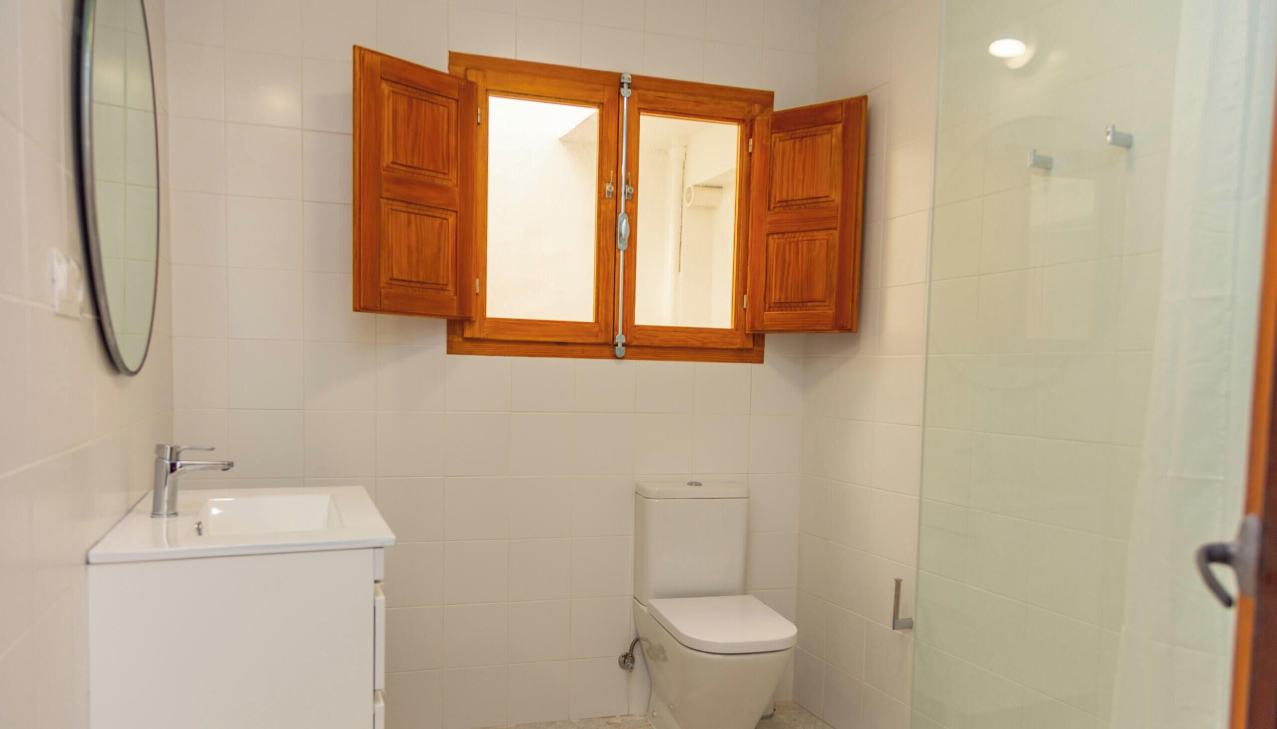 A bathroom with a white sink, a toilet, and a wooden cabinet above the mirror.