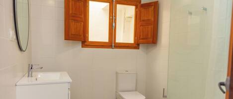 A bathroom with a white sink, a toilet, and a wooden cabinet above the mirror.