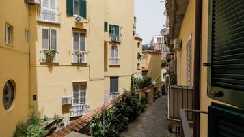 A narrow alleyway between yellow buildings with green shutters, potted plants, and a cobblestone path.