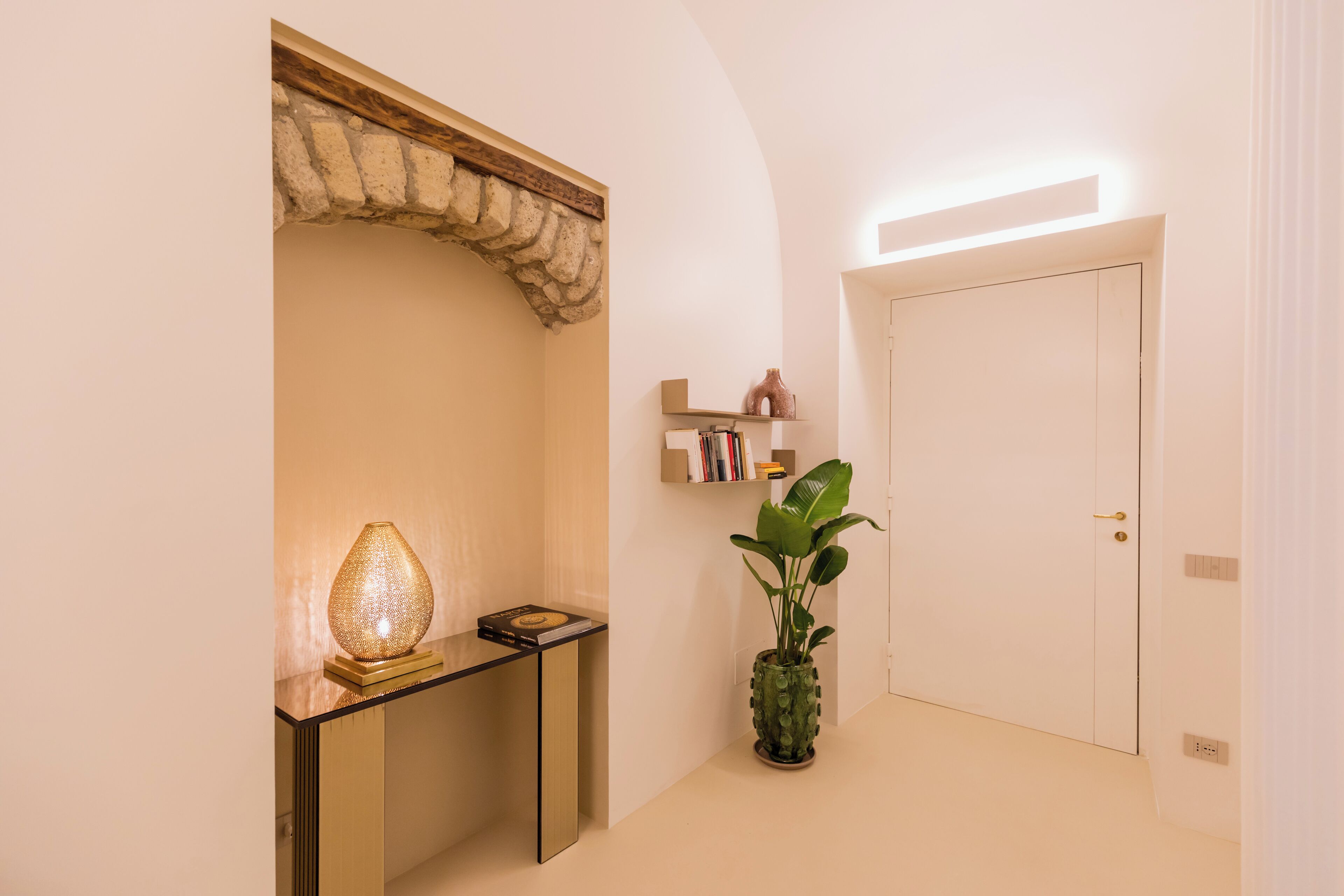 A hallway with a wooden archway, a small table with a lamp, a potted plant, and a closed door.