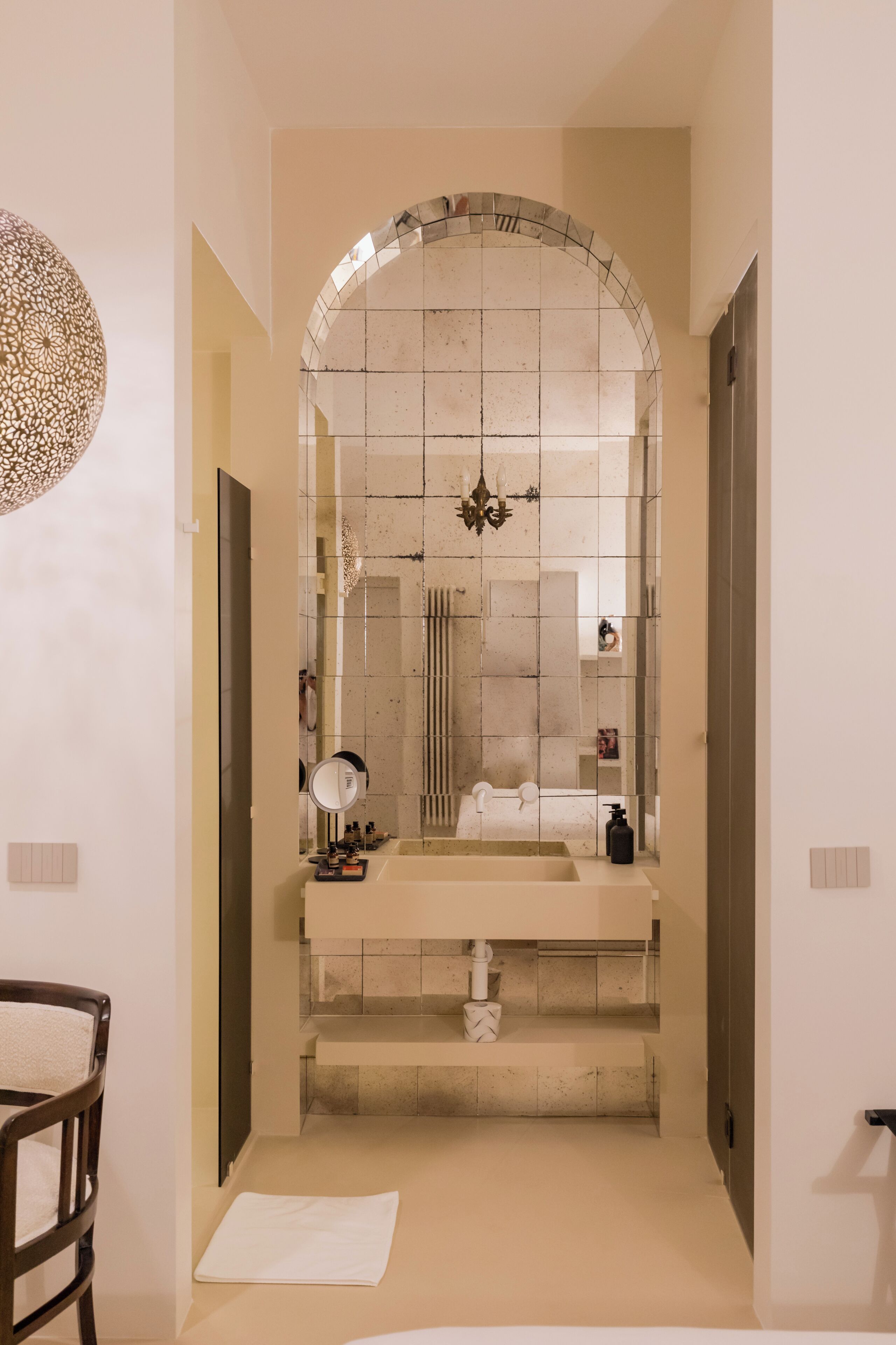 A narrow hallway leading to a bathroom with a large mirror, a sink, and a shower area.