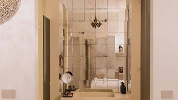A narrow hallway leading to a bathroom with a large mirror, a sink, and a shower area.