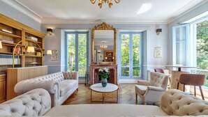 A spacious living room with a fireplace, a large mirror, and a view of greenery through large windows. - Château Les Alouettes (Cannes)