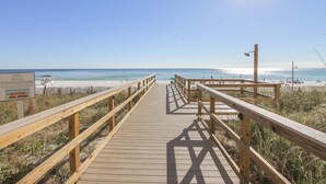 Un paseo marítimo de madera que lleva a una playa, con cielo despejado y sol.