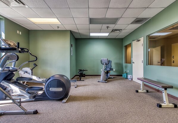 A gym with exercise equipment, a bench, and a door leading to another room.