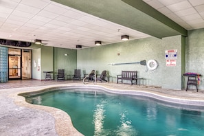 Une piscine intérieure avec un plongeoir, des chaises et un panneau indiquant la présence d’un sauveteur.