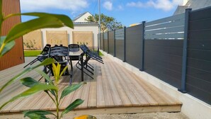 Un patio exterior con terraza de madera, una mesa y sillas, y una cerca negra.