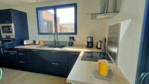 Cocina moderna con horno empotrado, microondas y lavaplatos. Hay una ventana sobre el lavaplatos y una cafetera en la encimera.