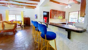 A bar area with stools, a wooden bar counter, and a kitchen in the background. - Mfalme Luxury Villas (Mtwapa)