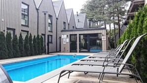 A swimming pool with lounge chairs, surrounded by buildings with modern architecture and a covered area. - Apartment In The Forest (Palanga)