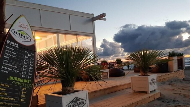 A beach bar with a menu board, outdoor seating, and potted plants. - Apartment In The Forest (Palanga)