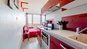 Una cocina compacta con muebles rojos, horno empotrado y lavamanos.