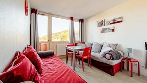 Una habitación con una cama, una mesa de comedor con sillas, una mesita con lámpara y vistas al exterior.