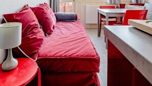 Una habitación con un sofá rojo, una mesita con una lámpara y un comedor con sillas rojas.