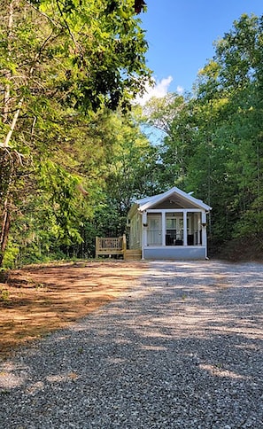 Situated in a wooded area, this cabin offers a peaceful retreat with a front porch and a gravel driveway.