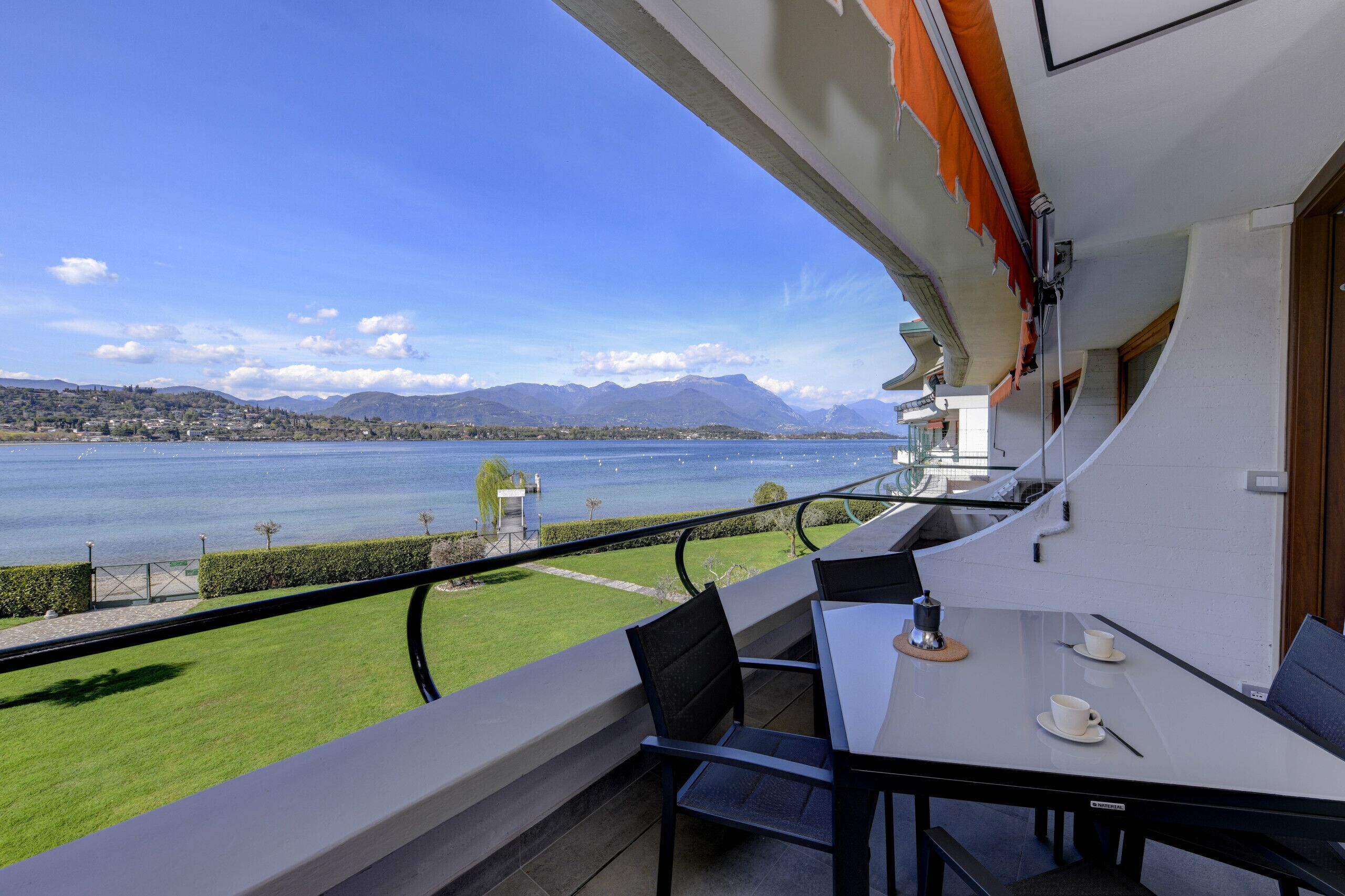 Varanda com mesa e cadeiras dando para um lago e montanhas.