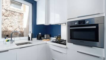 Een moderne keuken met witte kasten, een Bosch oven, een spoelbak en een raam met uitzicht op een stenen muur.
