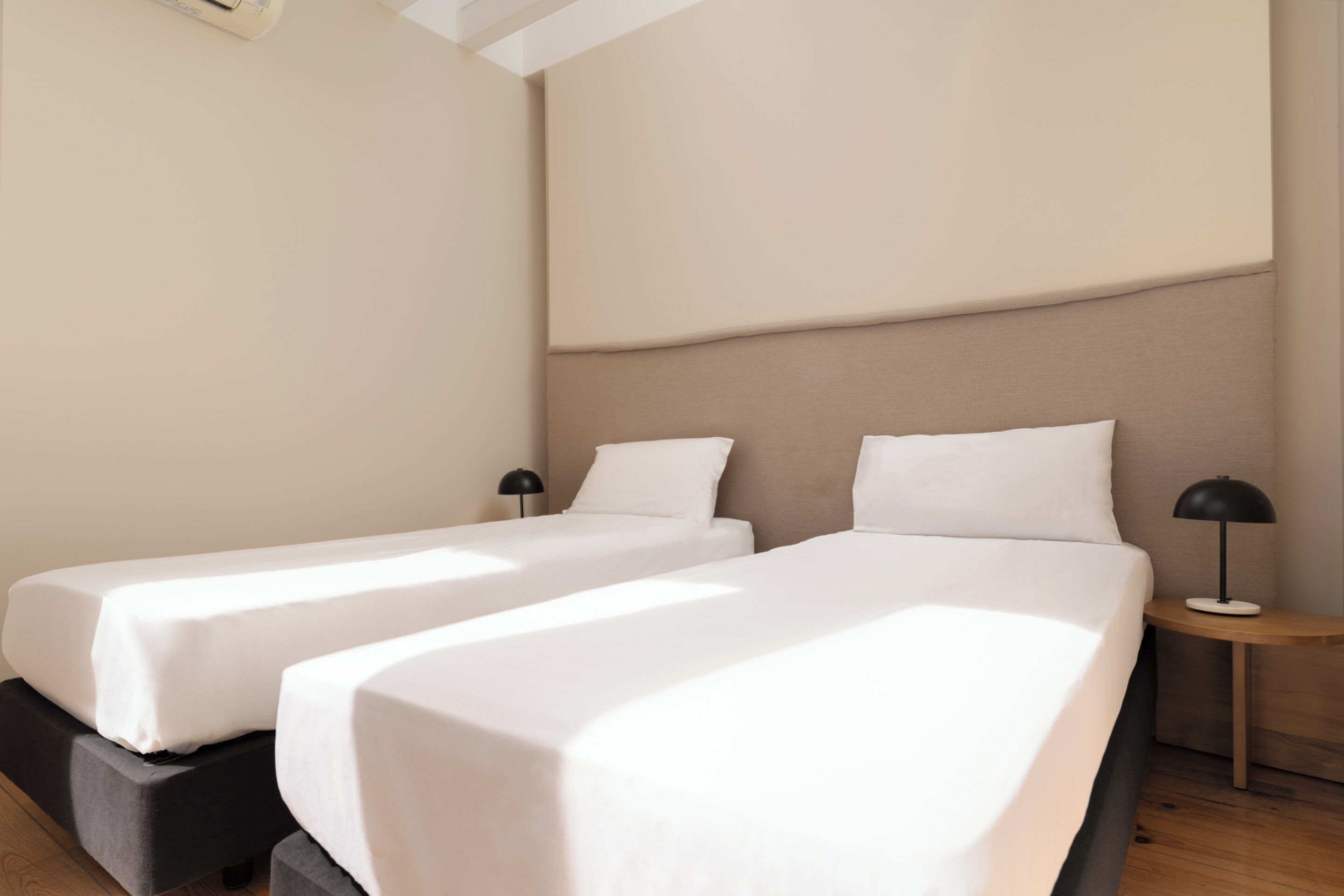 Ein Hotelzimmer mit zwei Betten, Holzboden und einem kleinen Nachttisch mit Lampe.