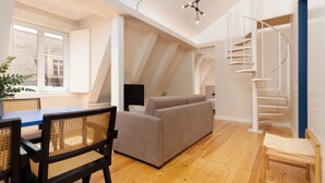 A spacious living area with a wooden floor, a sofa, a dining table with chairs, and a spiral staircase. - Limehome Lisbon Rua do Arsenal (Lisbon)