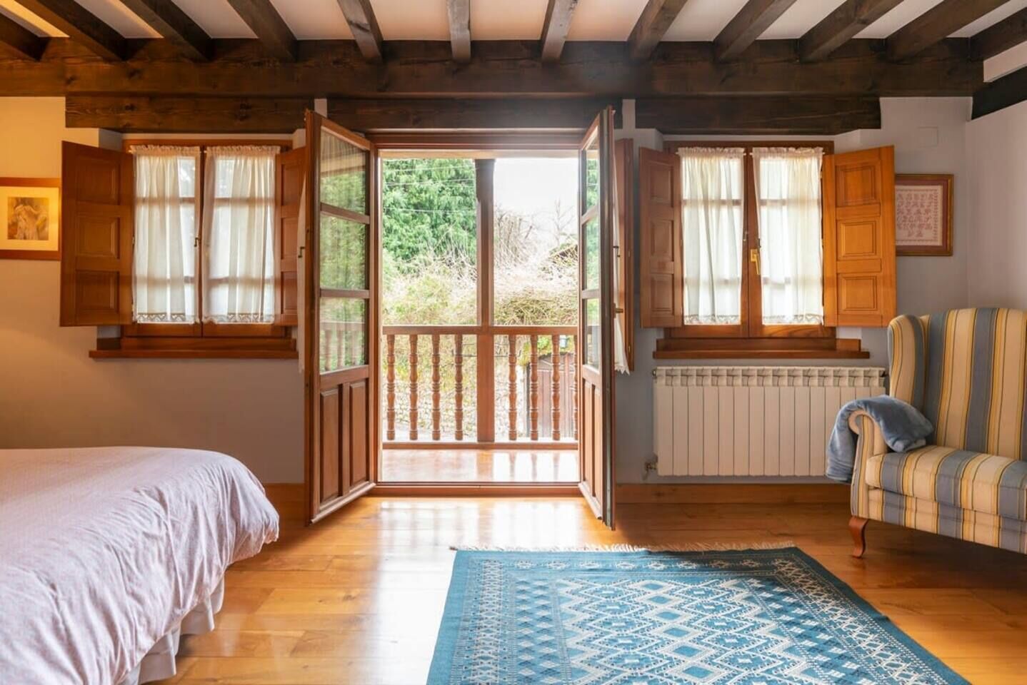 Una habitación con cama, una silla, ventana con cortinas, un radiador y vista a zonas verdes.