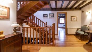 A wooden staircase with a railing leading to an upper floor, a patterned rug on the floor, and a chair with a lamp.