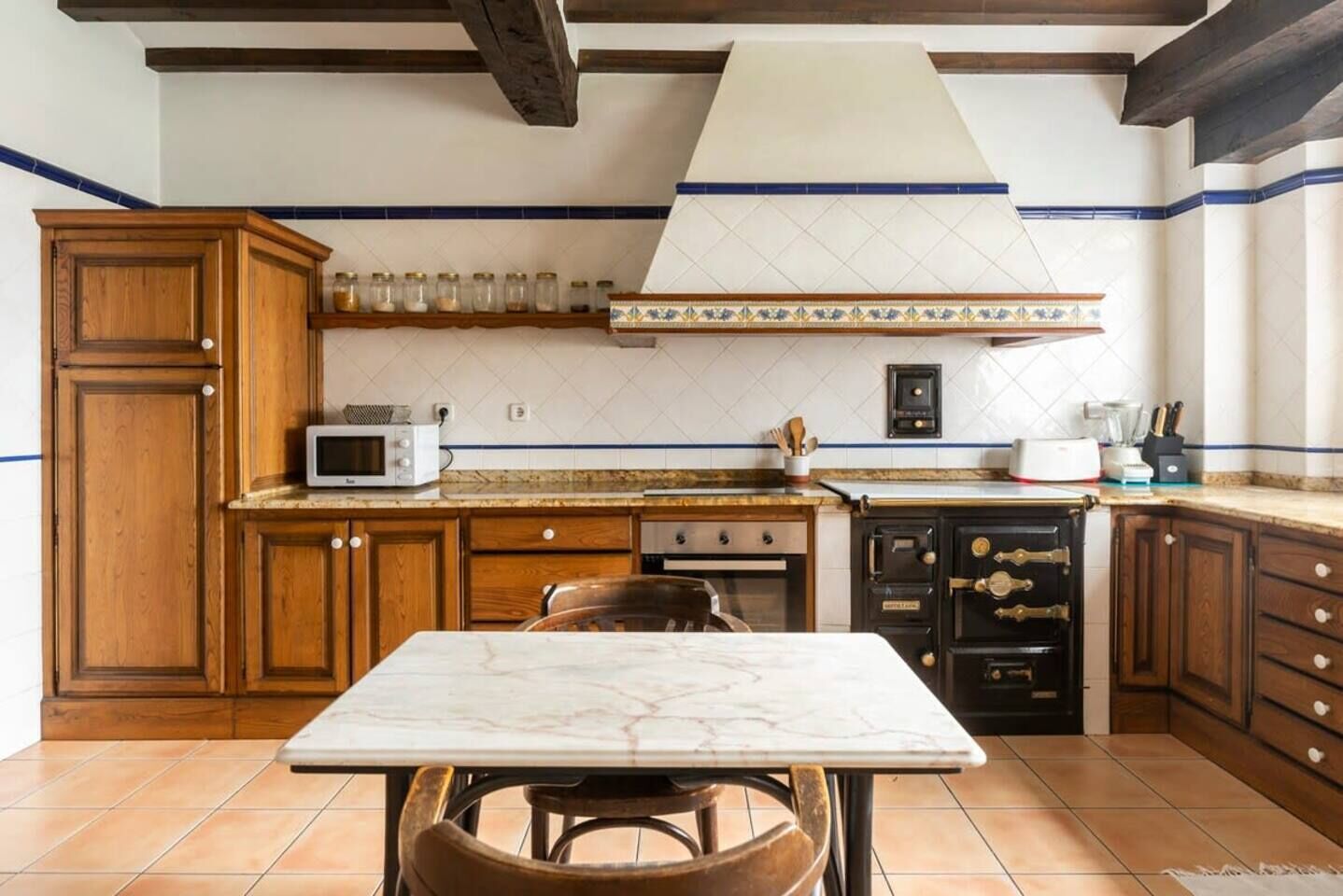 Une cuisine avec des meubles en bois, un plan de travail en marbre, un four à micro-ondes, une cuisinière et un évier.