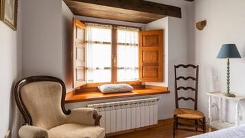Una habitación con asiento junto a la ventana, un radiador, una silla, una lámpara y una butaca de madera.