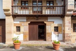 A building with a wooden balcony, a brown door, and two potted plants.