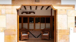 Une entrée d’immeuble avec une façade en pierre, deux chaises en osier et un sol carrelé.