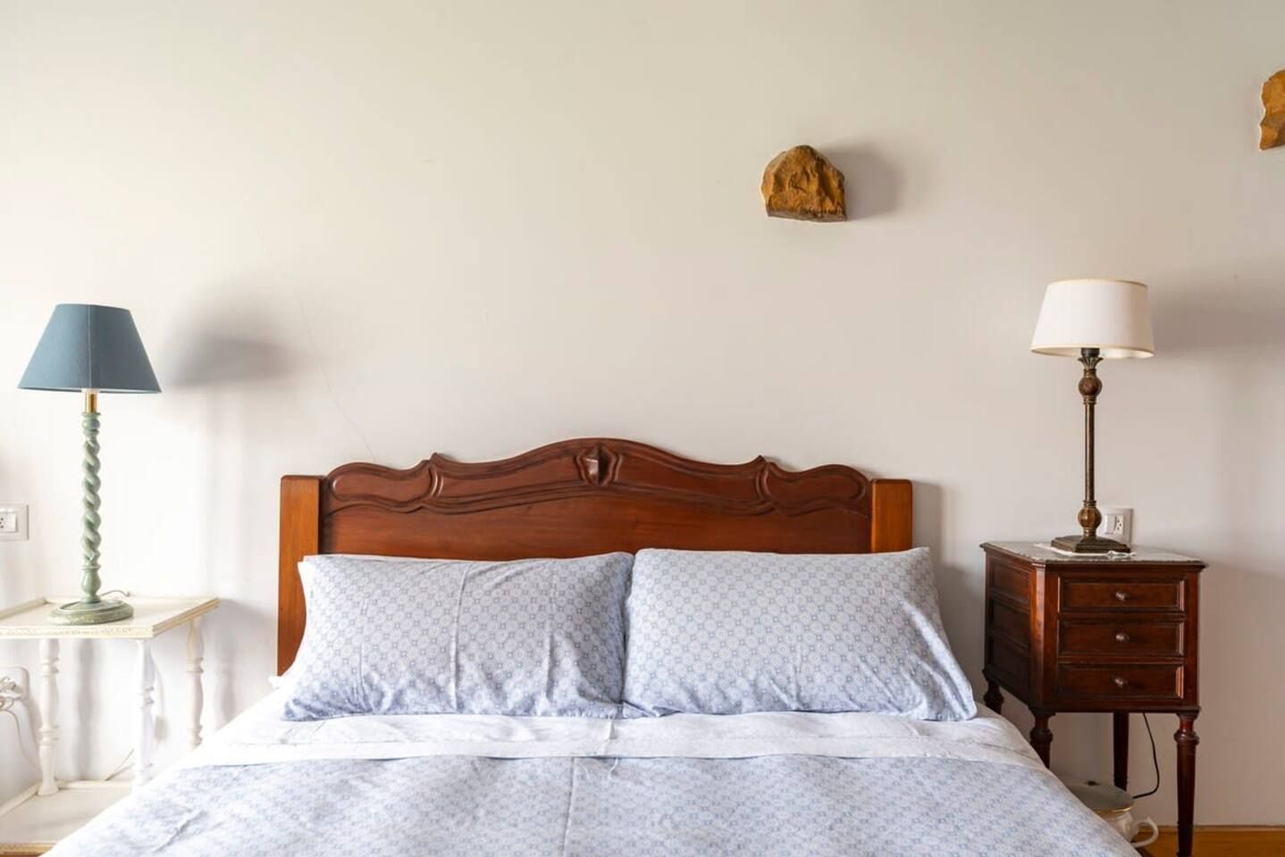 A bed with a wooden headboard, two pillows, a bedside table with a lamp, and a nightstand with a lamp.