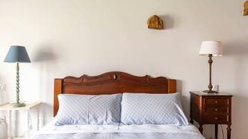 A bed with a wooden headboard, two pillows, a bedside table with a lamp, and a nightstand with a lamp.