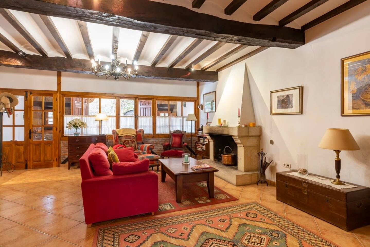 Una sala de estar acogedora con chimenea, vigas de madera y un amplio ventanal.