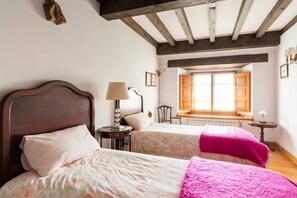Een slaapkamer met twee bedden, een raam met luiken, een kleine tafel met een lamp en een stoel.