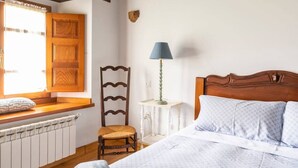 Une chambre à coucher avec une tête de lit en bois, une table de chevet avec une lampe, une chaise et une fenêtre avec des volets en bois.