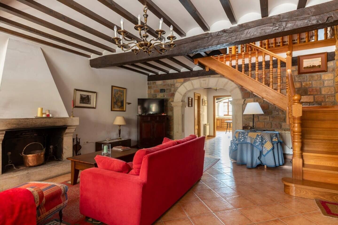 Un soggiorno tradizionale con camino, divano rosso, scala in legno e pareti in pietra.