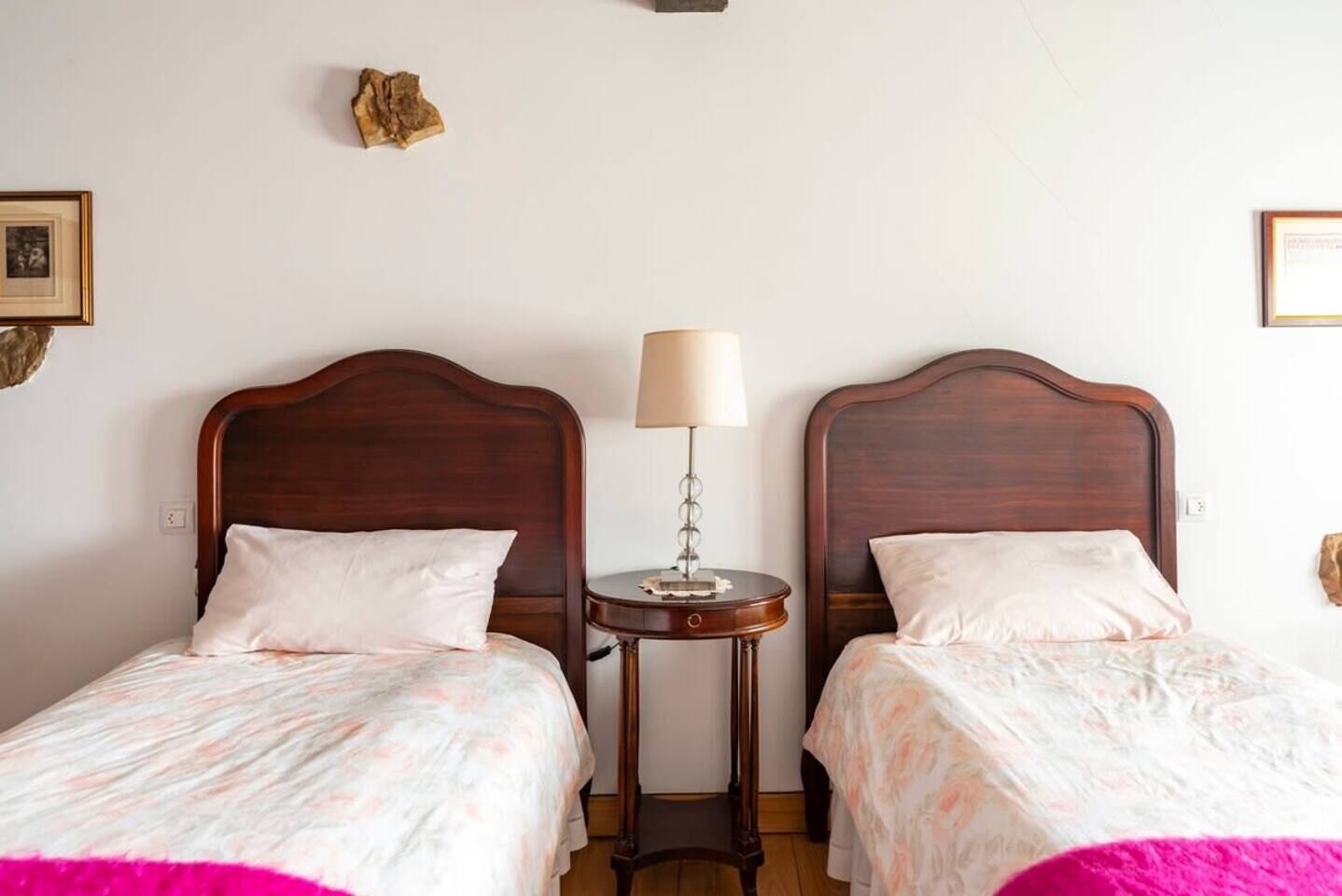 Une chambre d’hôtel avec deux lits en bois, une table de chevet avec une lampe et un petit objet décoratif accroché au mur.