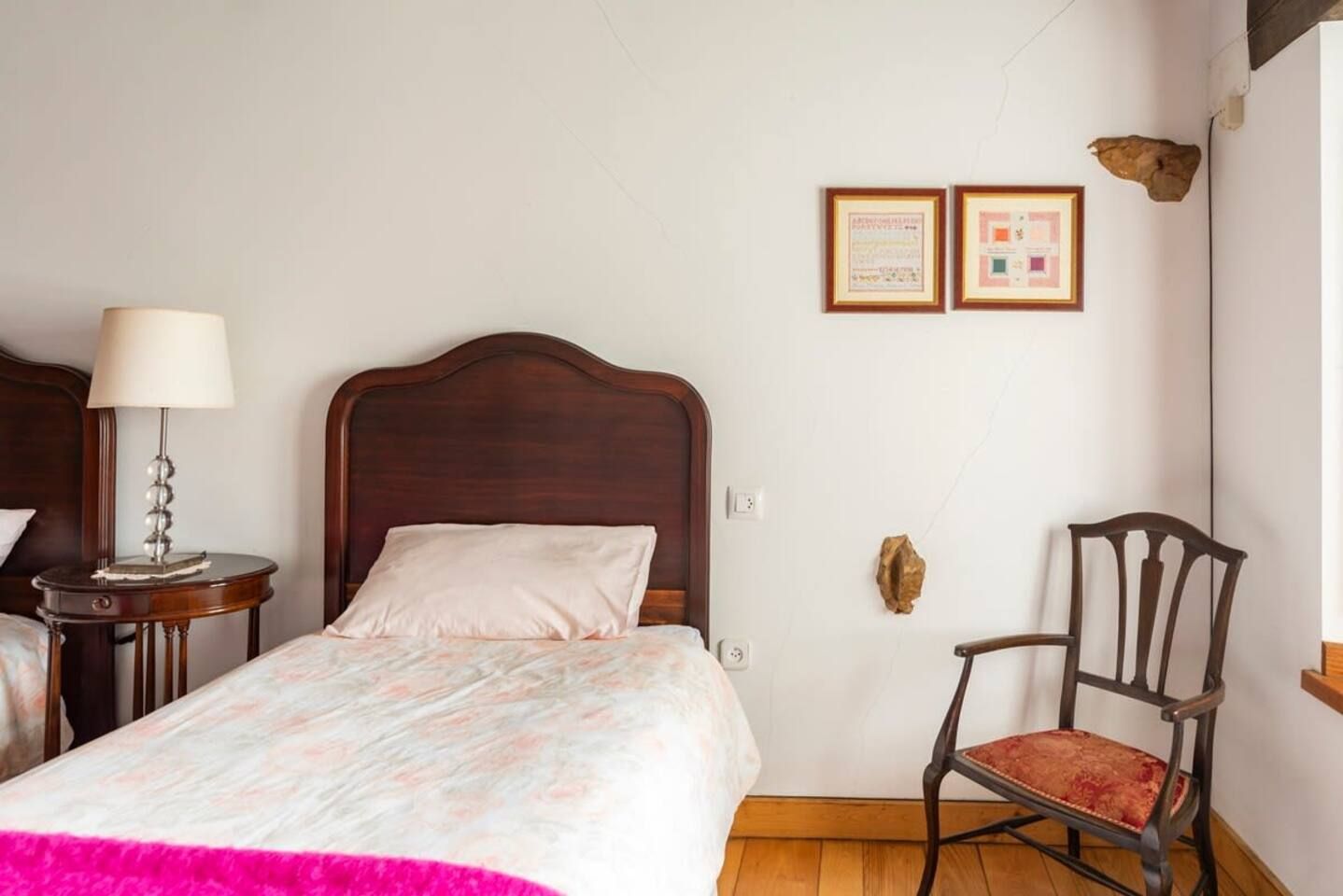 Una camera d'albergo con un letto di legno, un comodino con una lampada, una sedia e due certificati appesi alla parete.