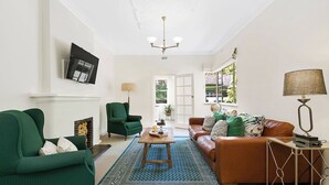 A living room with a fireplace, green armchair, brown sofa, and a blue patterned rug. - Charming Apartment | Malvern East (Malvern East)