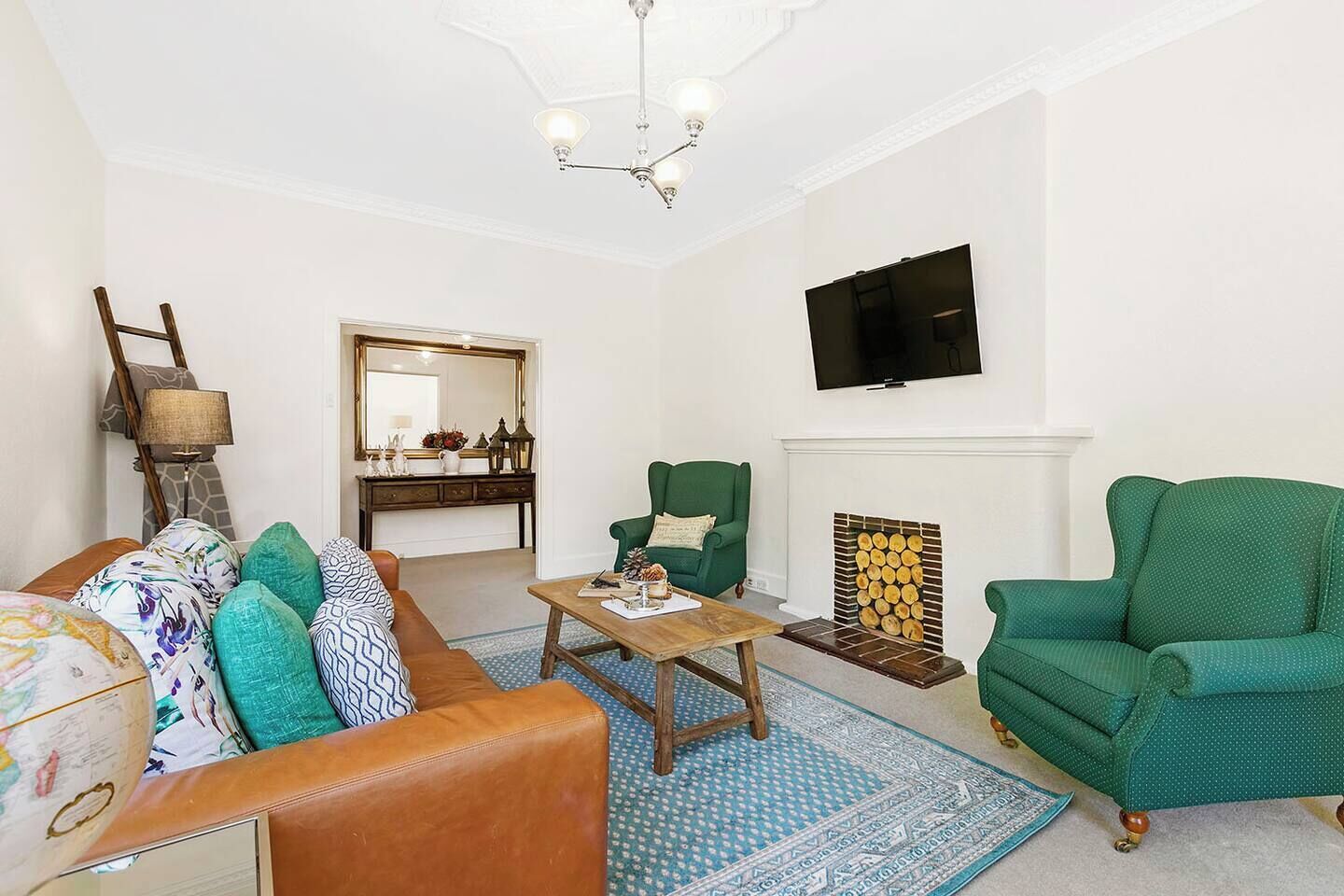 A living room with a sofa, armchairs, a coffee table, a fireplace, a television, and a mirror.