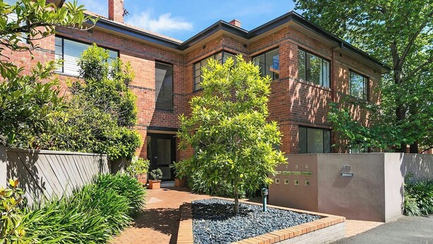 A two-story brick building with a landscaped front yard, including a small tree and a gravel area. - Charming Apartment | Malvern East (Malvern East)