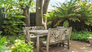 A wooden bench with a table in a garden setting. - Charming Apartment | Malvern East (Malvern East)