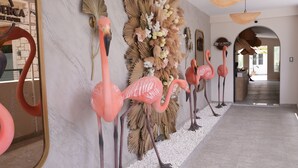 Een hal met een rij roze flamingo’s, een spiegel en een wand versierd met gedroogde planten en bloemen.