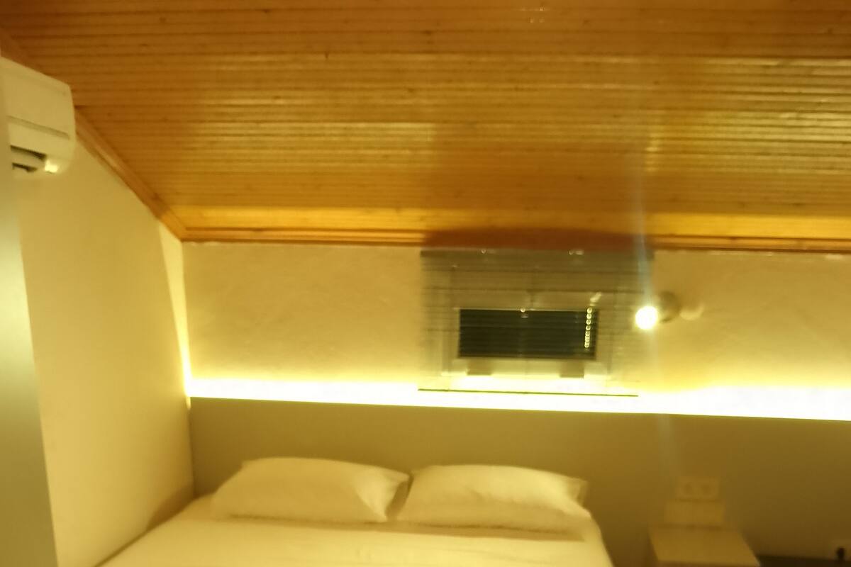 Een slaapkamer met een bed, een nachtkastje en een raam met een lamp erboven.