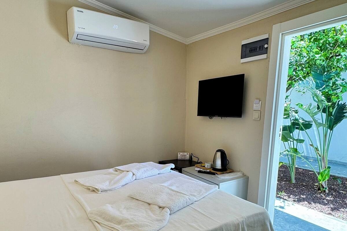 Hotelkamer met een bed, een flatscreen televisie, een airconditioner, een koffiezetapparaat en uitzicht op groen.