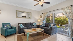 A living room with a ceiling fan, two sofas, a coffee table, and a view of the outdoors.