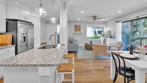 Una cocina moderna con encimera de granito, electrodomésticos de acero inoxidable, iluminación colgante y un comedor con mesa y sillas de vidrio.