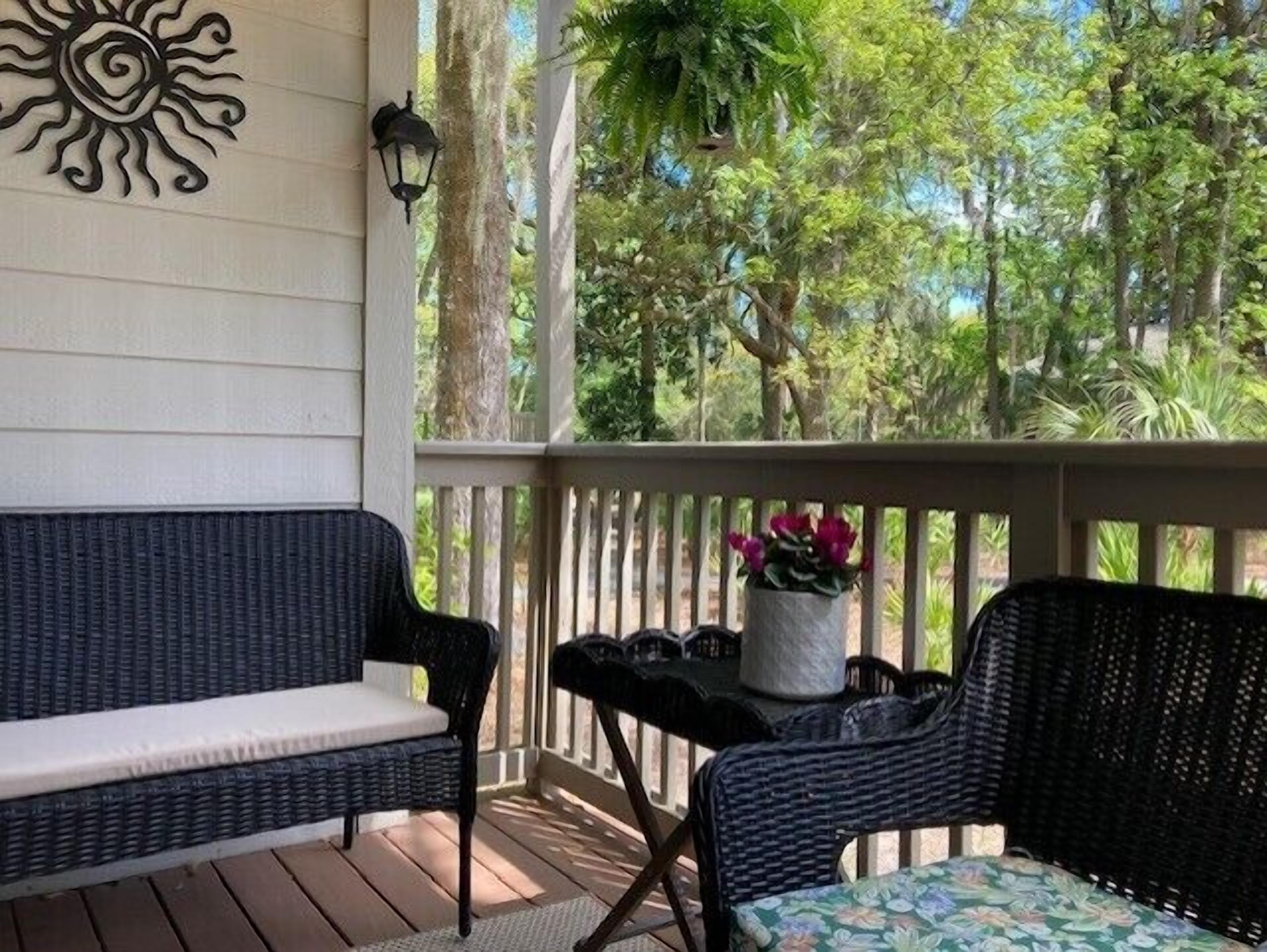 A covered porch with wicker furniture, a potted plant, and a decorative sun motif on the wall.